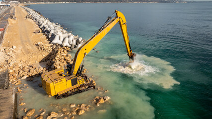 Waterfront construction site with excavator. Excavator working on a breakwater construction