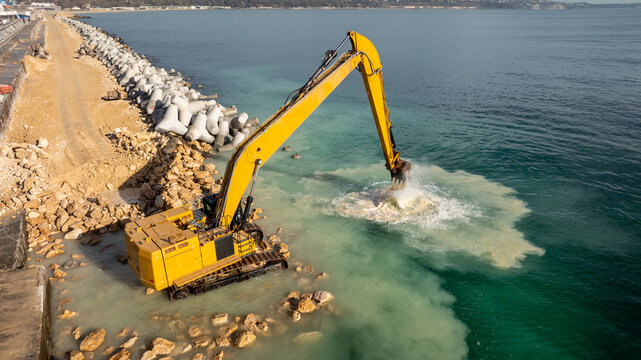 Waterfront construction site with excavator. Excavator working on a breakwater construction