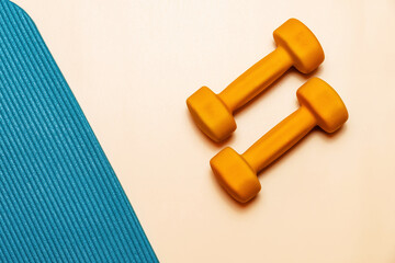 Two orange dumbbells and a blue yoga mat on a pastel pink background