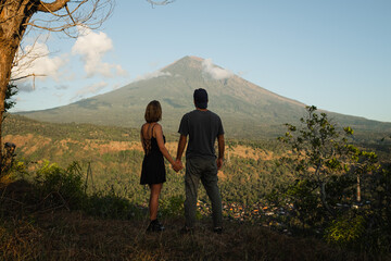 Fototapeta premium Couple Holding Hands with View of Mount Agung at Sunrise.