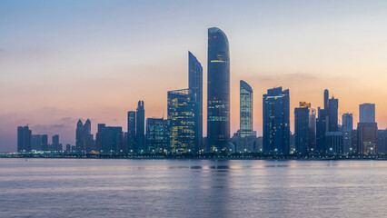 Fototapeta premium Abu Dhabi city skyline with skyscrapers before sunrise with water reflection night to day timelapse