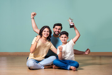 Indian boy or girl holding a trophy, celebrated by proud parents standing beside in a joyful moment
