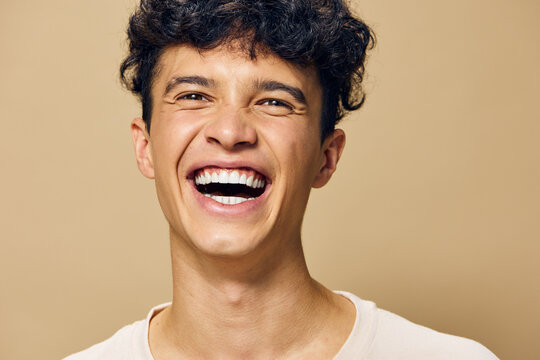 Smiling young man with curly hair against a beige background, showcasing joy and happiness, perfect for lifestyle and emotion related themes