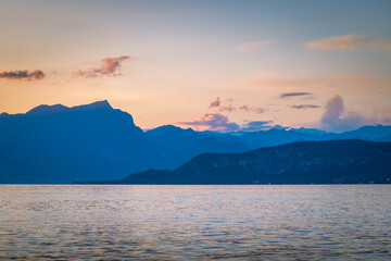Lake Garda with mountains in background at sunset, view from Lazise town shore, Italy, Europe.