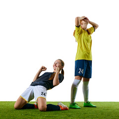Young female soccer players, one kneeling and celebrating joyfully, other standing with hands on head, both reacting to critical moment on field. Concept of sport, competition, tournament, game, event © Lustre Art Group 