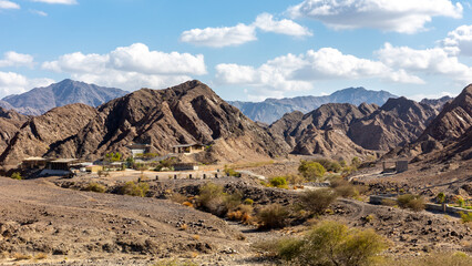 Landscape view of Wadi Shawka  dry riverbed with ‏Emirates Adventures camp buildings, rocky Hajar Mountains in the background, United Arab Emirates.
