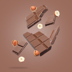 Pieces of tasty chocolate and hazelnuts falling on pale brown background