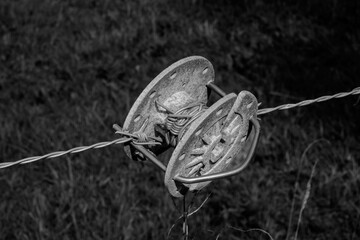 Black and white photo of barbed wire being tensioned with a round cable tensioner.