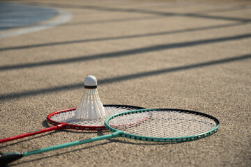 White badminton shuttlecock and badminton rackets on floor sport badminton court in sunny shadow....