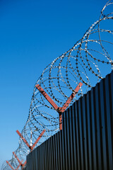 brown fence with barbed wire, prison or guarded area against blue sky