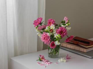 A bouquet of garden flowers, a laptop, notebooks on a white table