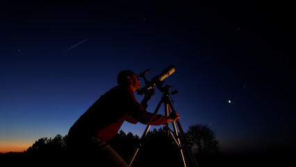 Amateur astronomer looking at the evening skies, observing planets, stars, Moon and other celestial objects with a telescope.