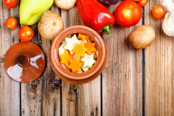 Traditional rustic home vegetable ragout with raw vegetables and spices in clay pots on an old vintage wooden table.