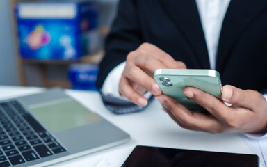 Businesswoman hand with a mobile phone over a laptop, Workplace at home, Freelancer, Working sitting in office at home, Online shopping and payments, Ecommerce and secure mobile banking concept.