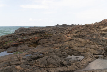 View of dark sea rocks against the ocean and cloudy sky. Preserved nature.