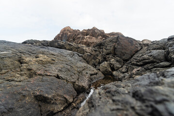 View of dark sea rocks against the ocean and cloudy sky. Preserved nature.