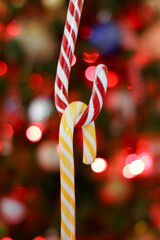  two candy canes, one red and white, the other yellow and white, intertwined against a blurred background of Christmas lights, creating a festive holiday atmosphere.