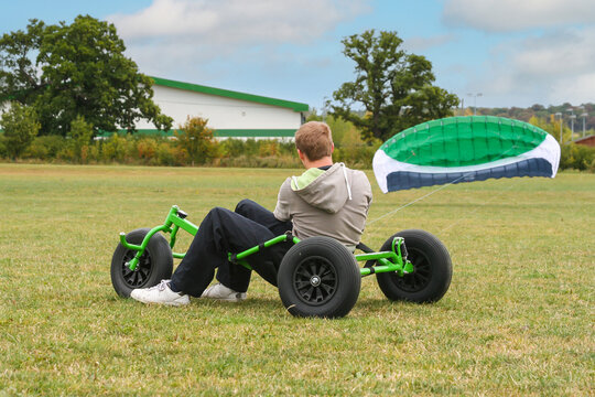 Extreme sports, kite buggy riding, young man prepares to launch enormous kite and use it to race his buggy across the open field using wind power to make it move at speed and his skills to direct and 