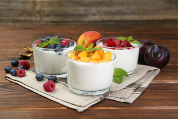 Tasty yogurt with fresh berries, fruits and mint in glasses on wooden table, closeup