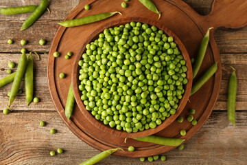 Fresh green peas in bowl and pods on wooden table, flat lay