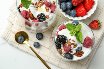 Tasty yogurt with fresh berries, granola and mint in glasses served on white table, flat lay