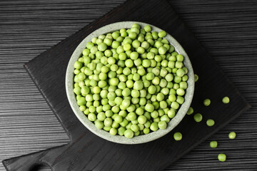 Fresh green peas in bowl on black wooden table, top view