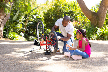 Fixing bicycle, father and daughter bonding outdoors in sunny park
