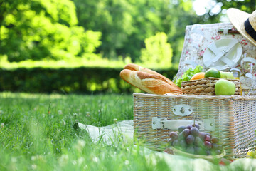 Picnic wicker basket with delicious food on green grass outdoors, space for text