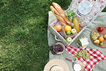 Picnic wicker basket with delicious food and drink on blanket outdoors, above view. Space for text