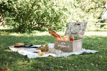 Picnic wicker baskets with delicious food, tableware and drink on blanket outdoors