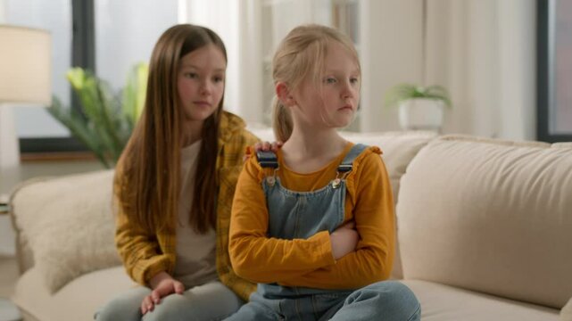 Upset angry little Caucasian children girls sisters kids friends quarrel daughters apology ask for forgiveness feeling guilty touch calming down offended ignore family argument problems at home couch