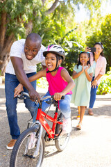 Teaching daughter to ride bicycle, father guiding while mother and sister watching