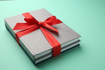 Books tied with red ribbon on green background, closeup. Perfect gift