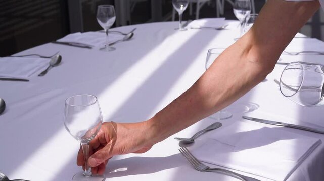 Shot of waiter hand preparing dinner table for celebration at banquet hall or restaurant table outdoors on a summer day. Beautiful Table setting.