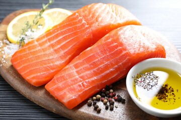 Pieces of fresh salmon with thyme, lemon, oil and spices on black table, closeup