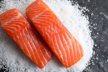 Pieces of fresh salmon and salt on dark textured table, top view