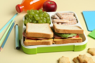 Lunch box with snacks, bottle of juice and stationery on yellow table, closeup