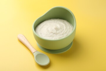 Delicious baby food in bowl and spoon on yellow background
