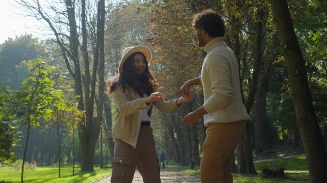 Positive married Indian Arabic couple girlfriend lady wife cheerful happy boyfriend guy husband spinning boy girl dancing together woman female man male touch in park sunshine romance tenderness love
