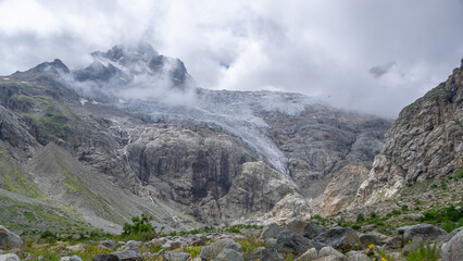 View of a glacier covered with clouds. Panorama in a mountain gorge. The glacier descends from the...