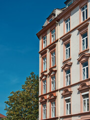 Detail of a historic facade of an old building with beautiful windows, decoration, blue sky and a tree standing next to it