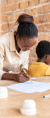 A focused woman writes notes at a table while a child sits nearby, highlighting a moment of learning and concentration.