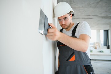Worker in uniform plastering wall with putty knife indoors