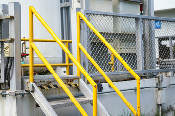 Refinery plant and oil storage metal walkway-stair platform with yellow handrail or banister rail part. Industrial workplace, close-up and selective focus.