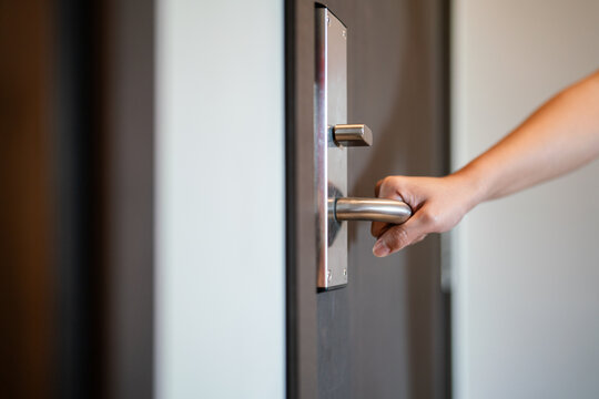Action of a human hand is holding on standless door lever handle to open the wooden door. close-up and selective focus.