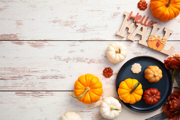 Flat lay composition with plaid, plate with pumpkins, Hello Fall message on wooden desk table top view.
