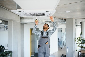 Indian male worker inspecting the air conditioner mounted on the ceiling