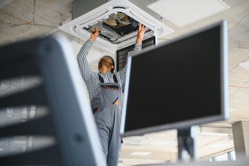 Indian male worker inspecting the air conditioner mounted on the ceiling