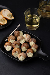 Escargot bourguignon with butter and garlic. Traditional French dish made from snails, served with baguette and white wine. Selective focus, close-up, black background.