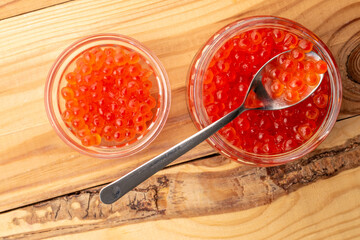 Red caviar in a glass jar with a spoon on a wooden table, macro, top view.